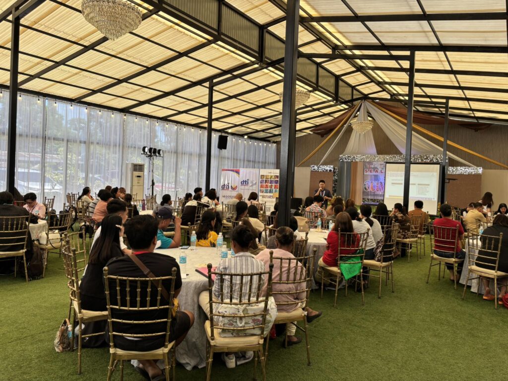 Audience attending the S.E.A.L. to S.E.G.A. entrepreneurship event in Guimaras, seated at round tables inside a decorated indoor venue while a speaker presents on stage.